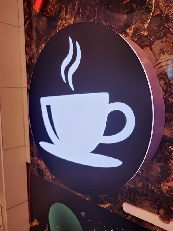 Round backlit coffee cup glow signage in a café
