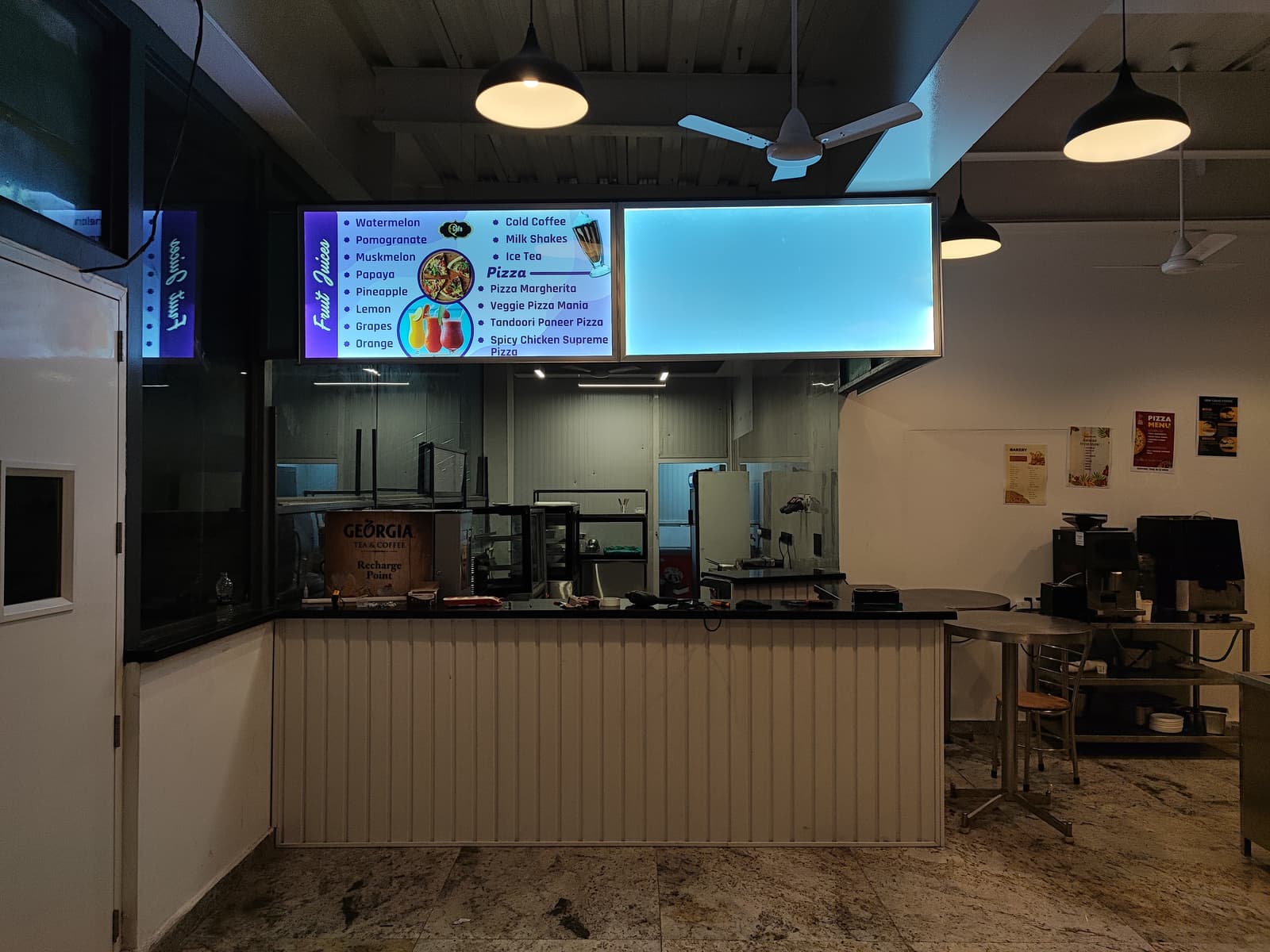 Fruit juices and pizza menu signage above a café counter